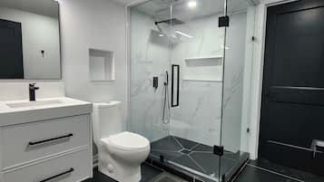 A modern bathroom with a glass-enclosed shower, a white toilet, and a vanity with drawers.