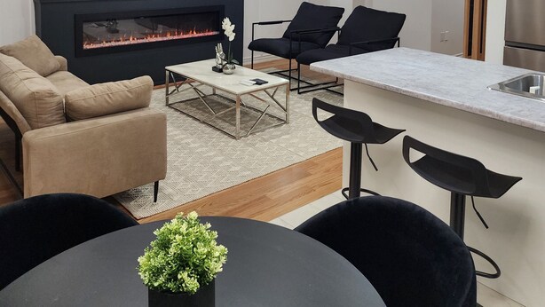 Een moderne woonkamer met een open haard, zwarte banken, een salontafel en een eethoek met een zwarte tafel en stoelen.