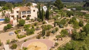 A large villa with a landscaped garden, including a circular patio and various trees.