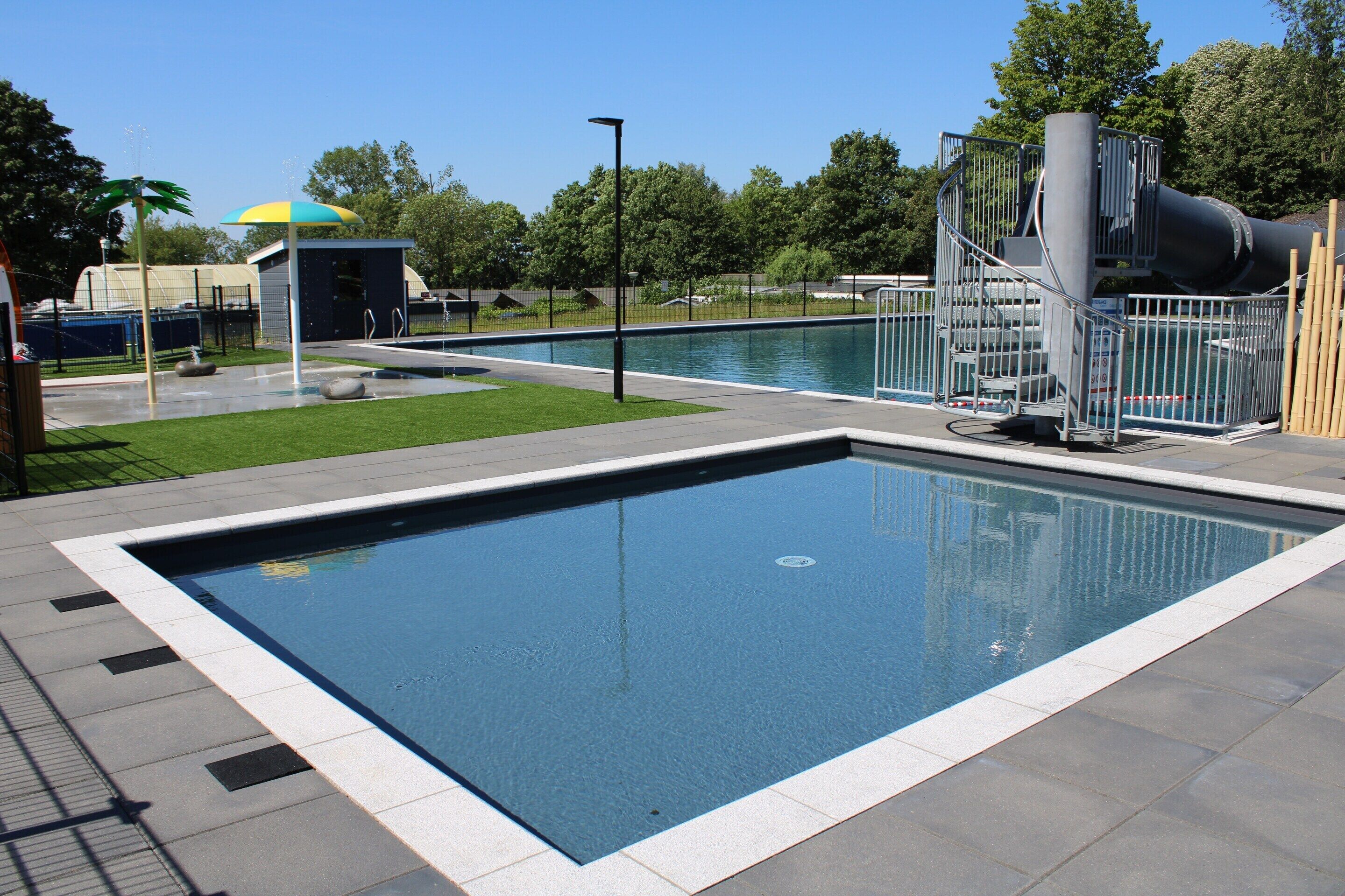 A swimming pool with a surrounding deck, a small building, and a water slide structure.
