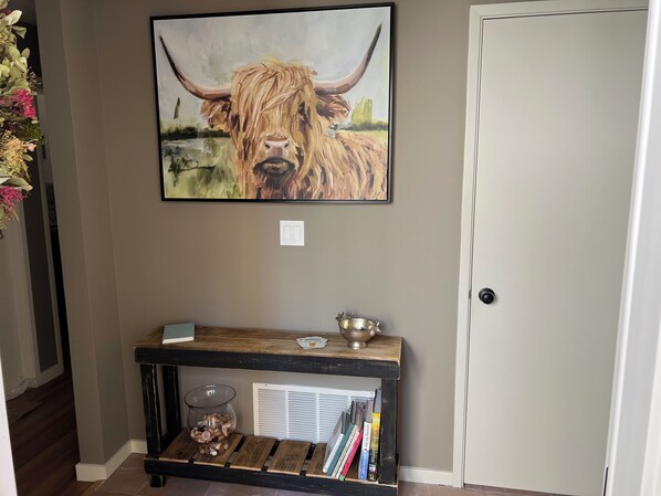 Un couloir orné d’un tableau représentant un yak, une console en bois sur laquelle reposent un bol et un récipient en verre, et une porte.