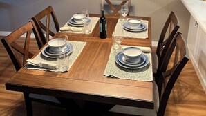 Una mesa de comedor dispuesta con platos, vasos y una botella, rodeada de sillas.
