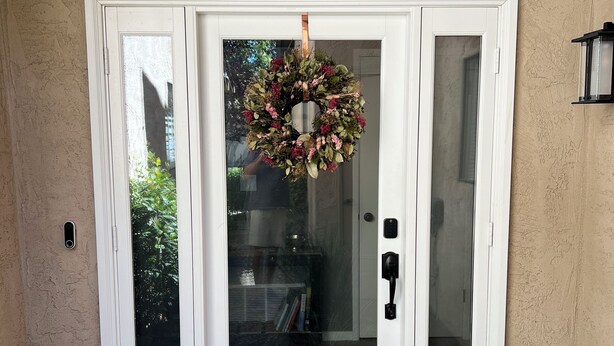 Puerta principal con panel de vidrio, corona decorativa y felpudo con el texto 'home sweet home'.