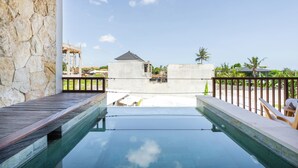 Un área de piscina con un muro de piedra, una terraza de madera y vistas a un edificio en construcción.
