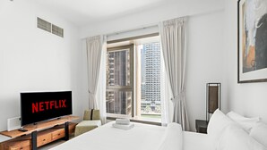 Een moderne hotelkamer met een groot bed, een televisie op een houten standaard, een raam met gordijnen en uitzicht op de stad.