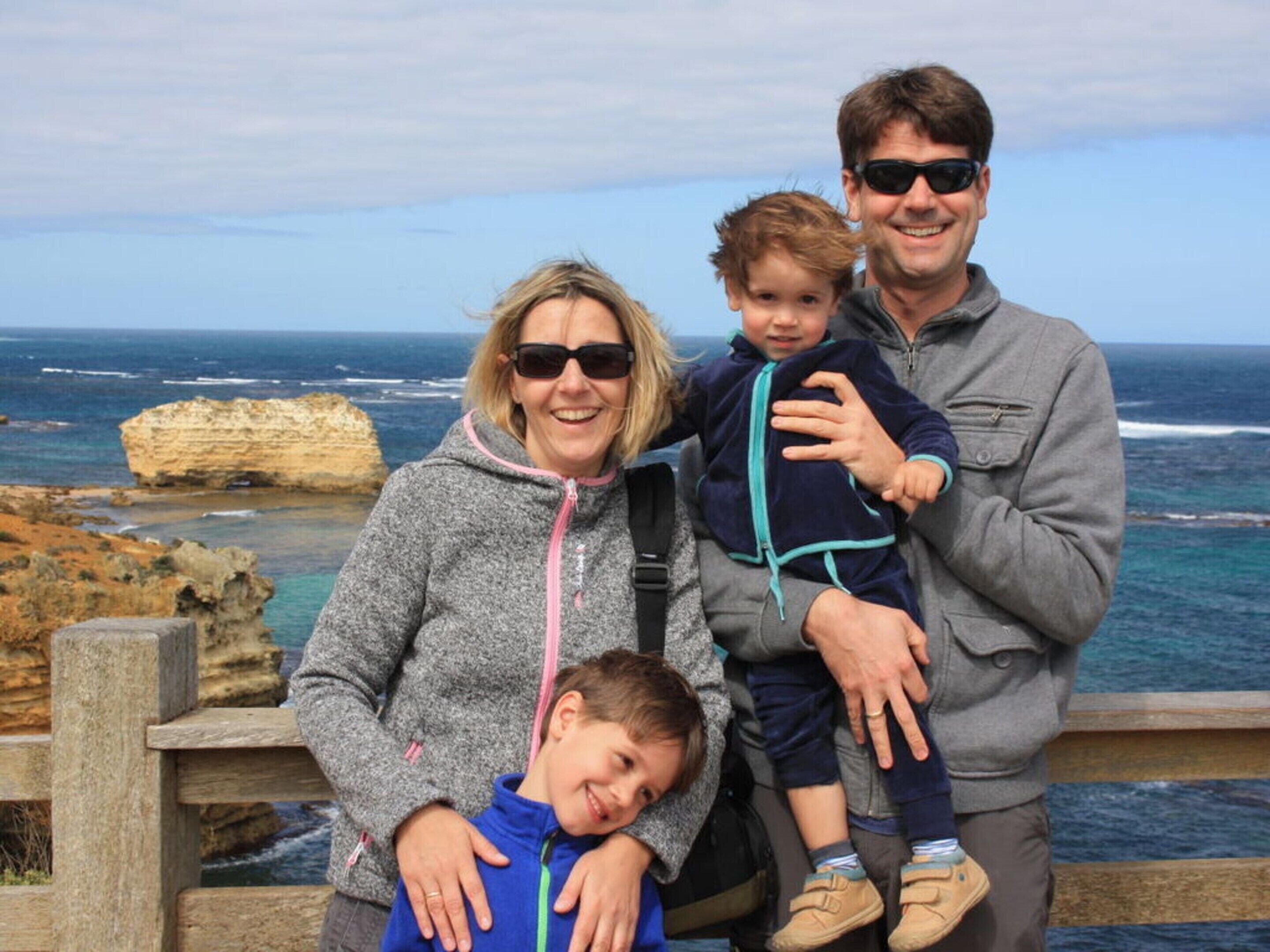 Una familia de cuatro personas en un mirador costero, con un acantilado rocoso y el océano al fondo.