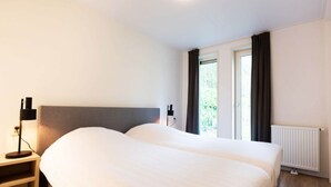 A hotel room with a large bed, bedside tables, a lamp, and a window with curtains. - Charming Apartment in Graach an der Mosel (Zorgvlied)