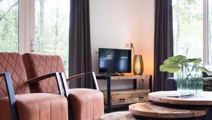 A modern living room with a leather sofa, a TV on a wooden stand, a small table, and a plant. - Charming Apartment in Graach an der Mosel (Zorgvlied)