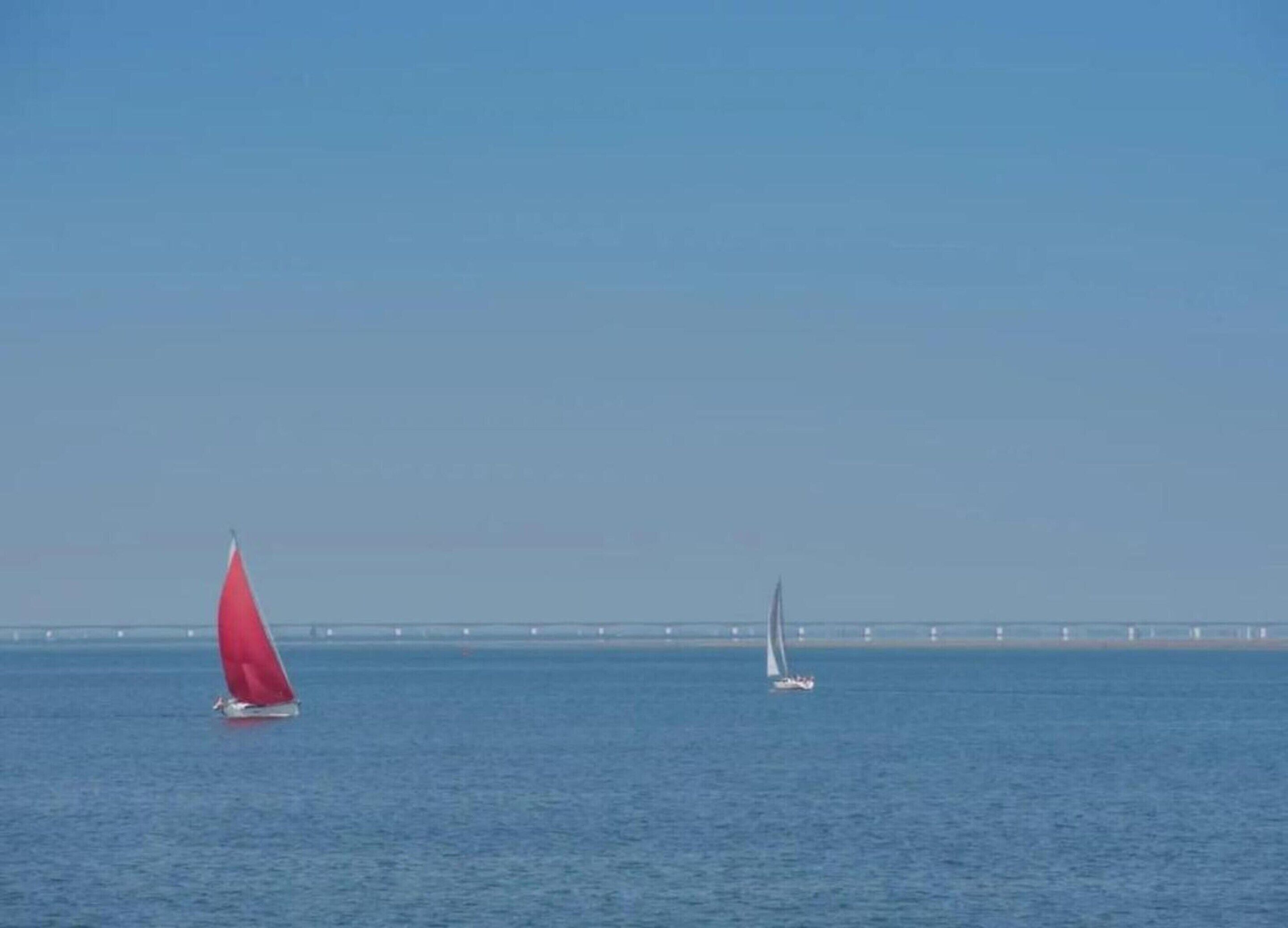 Two sailboats on calm water with a bridge in the background.