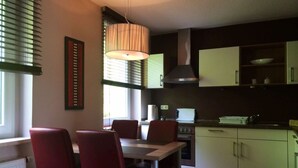 A modern kitchen with a dining area. It includes a table with chairs, a stove, a microwave, and cabinets. - Saaleland Apartment 3 (Schleiz)