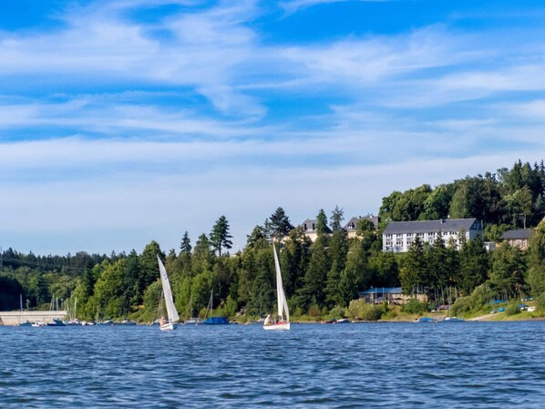 A coastal scene with sailboats on the water, a forested hill with buildings, and a clear sky. - Saaleland Apartment 3 (Schleiz)