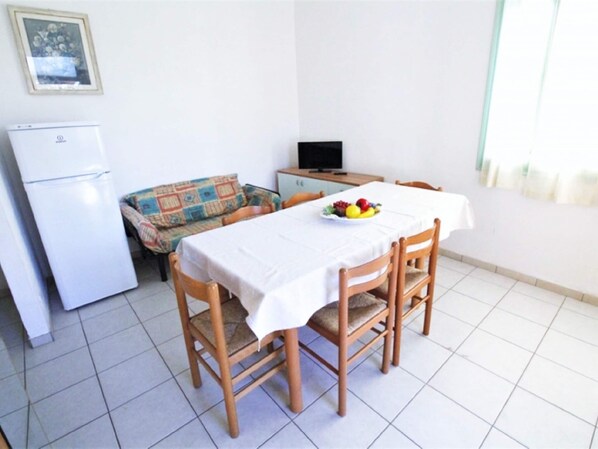 A dining area with a table set for four, a sofa, a refrigerator, and a television.