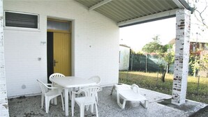 Ein weißes Gebäude mit überdachter Terrasse, an der ein Tisch und Stühle stehen.