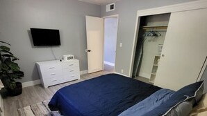 Ein Schlafzimmer mit Bett, Kommode, Fernseher und einer Pflanze.