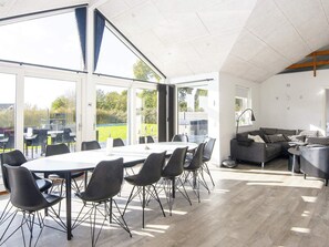 A spacious room with a large dining table, multiple chairs, a sofa, and a large window offering a view of the outdoors.