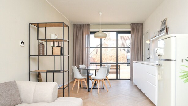 Une cuisine moderne avec un réfrigérateur blanc, une table à manger avec des chaises et une bibliothèque intégrée contenant divers objets.