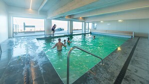 Une piscine intérieure offrant une vue dégagée sur l’extérieur, un banc placé le long du bord de la piscine et une personne prenant une photo.