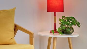 Een hoek van een kamer met een houten stoel, een witte bijzettafeltje met een rode lamp en een potplant.