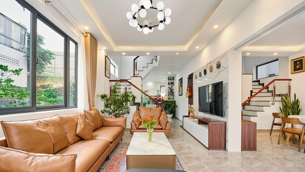 Un moderno salón con un sofá de cuero, una mesa de centro y un televisor. Se observa una escalera que conduce a otro nivel.