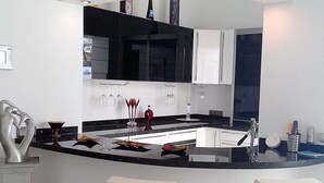 A modern kitchen with a curved island, white bar stools, and a black countertop. - Villa Amelie Comfortable Holiday Residence (Pajara)