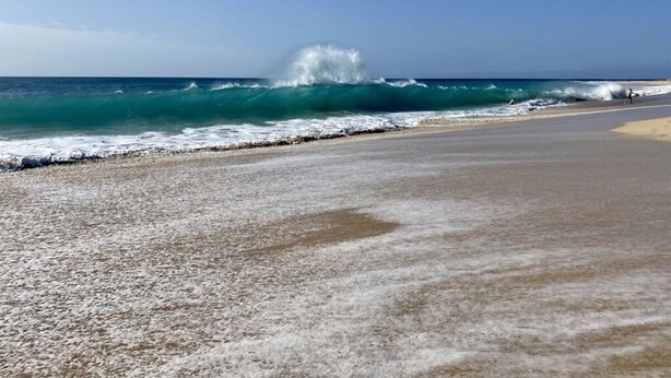 A beach with waves crashing onto the shore, a clear sky, and a few people walking along the beach. - Villa Amelie Comfortable Holiday Residence (Pajara)