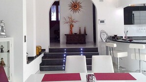 A modern kitchen with white cabinetry, a dining area with a red table runner, and a staircase leading to a living area. - Villa Amelie Comfortable Holiday Residence (Pajara)