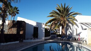 A pool area with a clear blue sky, palm trees, and white buildings. - Villa Amelie Comfortable Holiday Residence (Pajara)