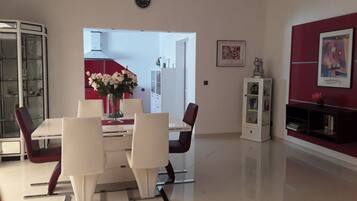 A modern dining area with a white table and chairs, a vase of flowers, and a red accent wall.