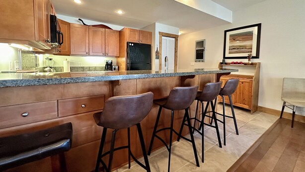 A modern kitchen with wooden cabinets, a granite countertop, and bar stools. - Lakefront Home away from Home (Osoyoos)