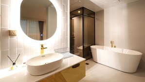 Un bagno moderno con una vasca freestanding, un ampio specchio ovale e un lavandino bianco.