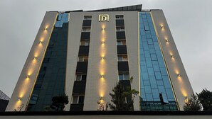 Un moderno edificio alberghiero con un logo 'D' ben visibile, diversi piani e finestre illuminate.