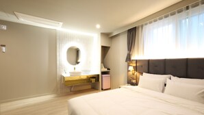 Una camera d'albergo moderna con un letto grande, uno specchio rotondo, un mobile toilette con lavandino e una finestra con tende.
