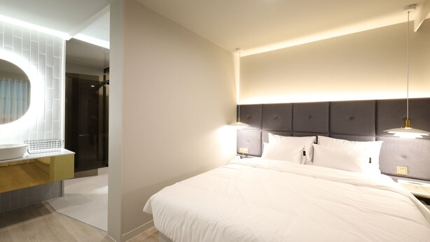 Una camera d'albergo moderna con un letto grande, lampade ai lati del letto e uno specchio circolare integrato.