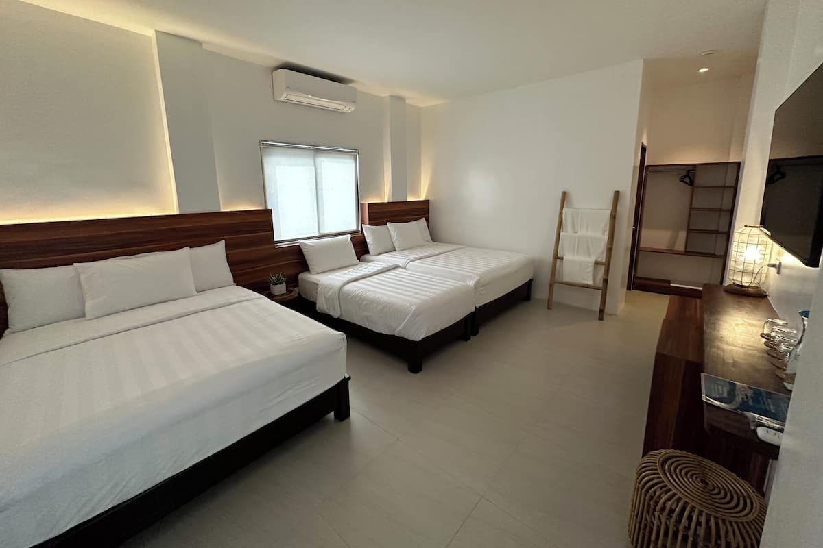 Habitación de hotel con dos camas, cabecero de madera, mesita de noche con una planta, aire acondicionado montado en la pared y una ventana con persianas.