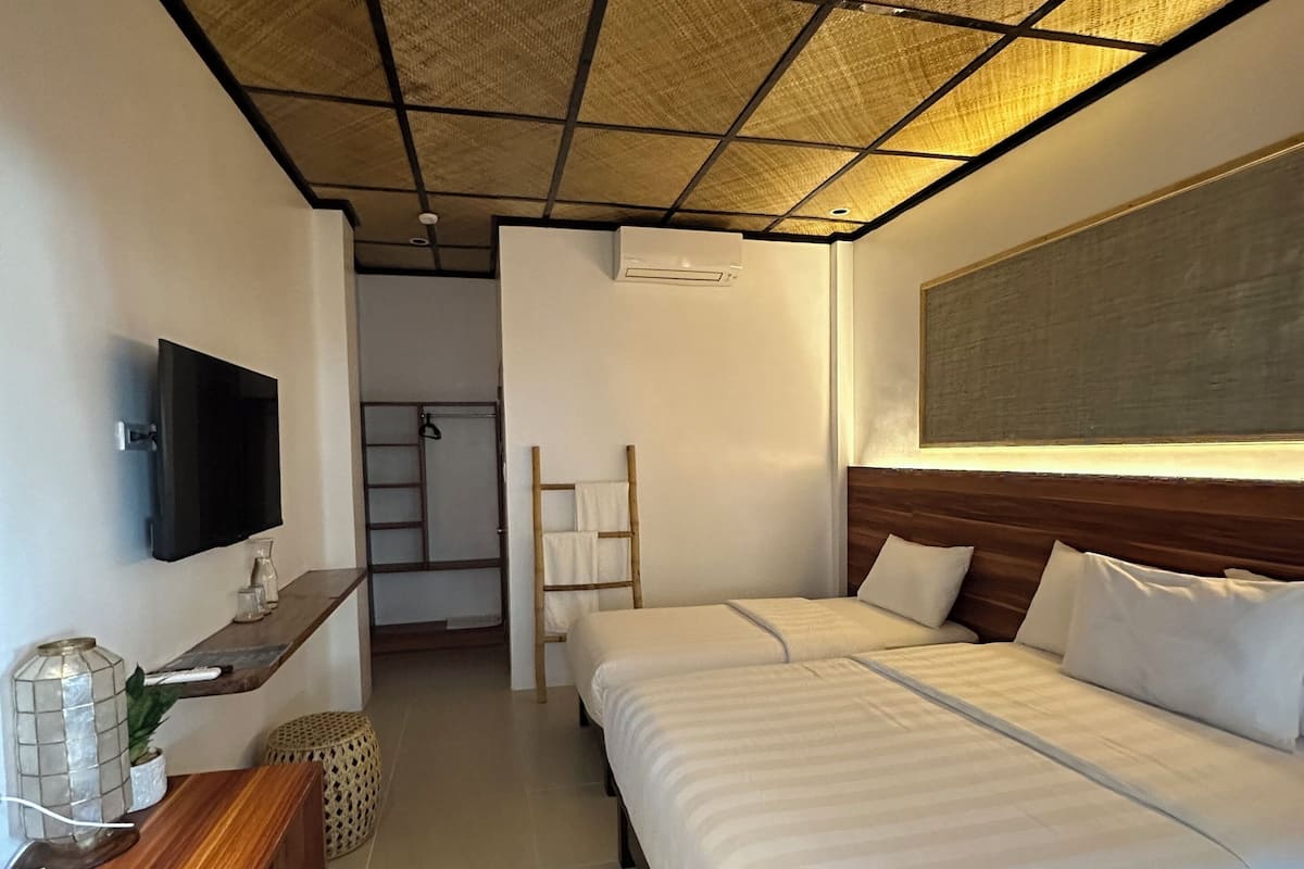 Una habitación de hotel con una cama grande, un televisor de pantalla plana montado en la pared, una mesita de noche de madera y un techo con diseño tejido.