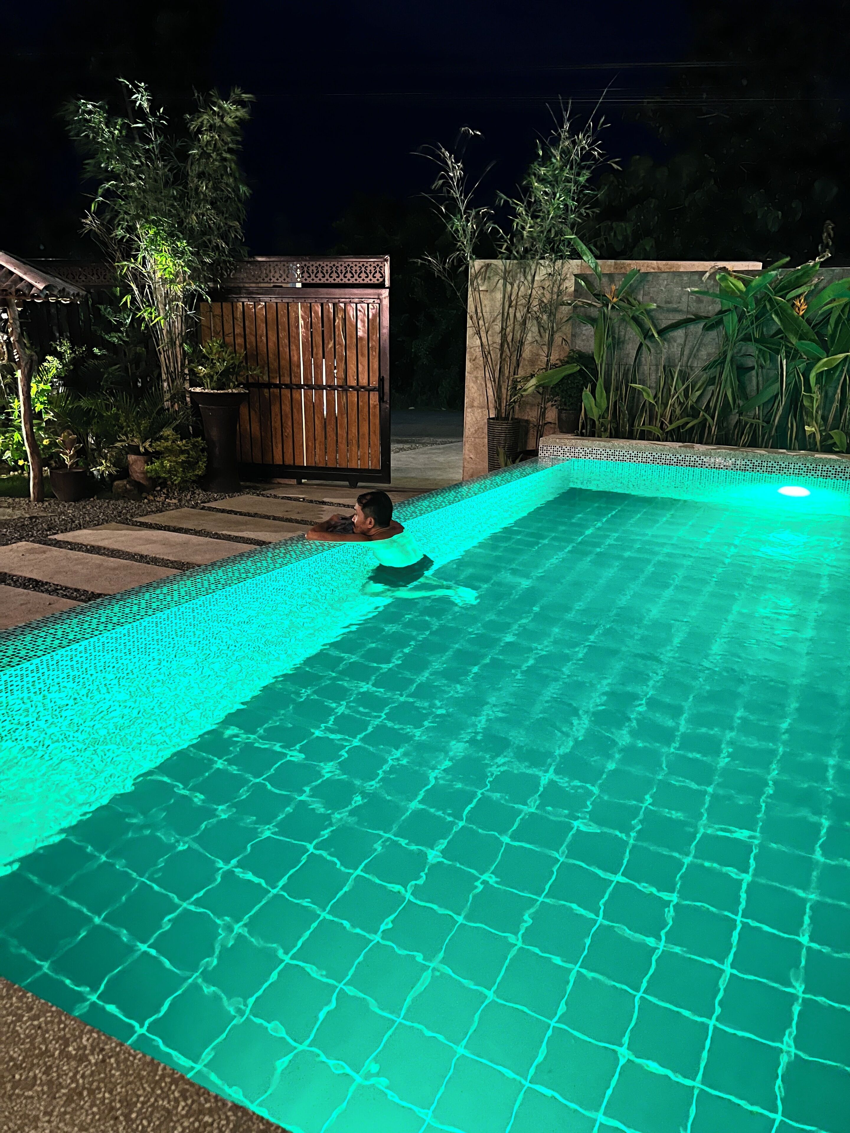 Une piscine dont le bord est recouvert de carreaux, et une personne se détend dans l’eau.