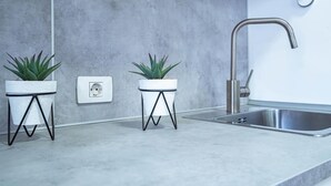 Een moderne keuken met een roestvrijstalen spoelbak, twee planten in potten op metalen standaardjes, en een witte stopcontact op de muur.