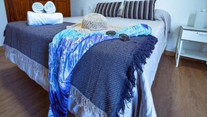 Een net opgemaakt bed met een deken met blauw-witte patronen, een gehaakte muts en zonnebril erop.