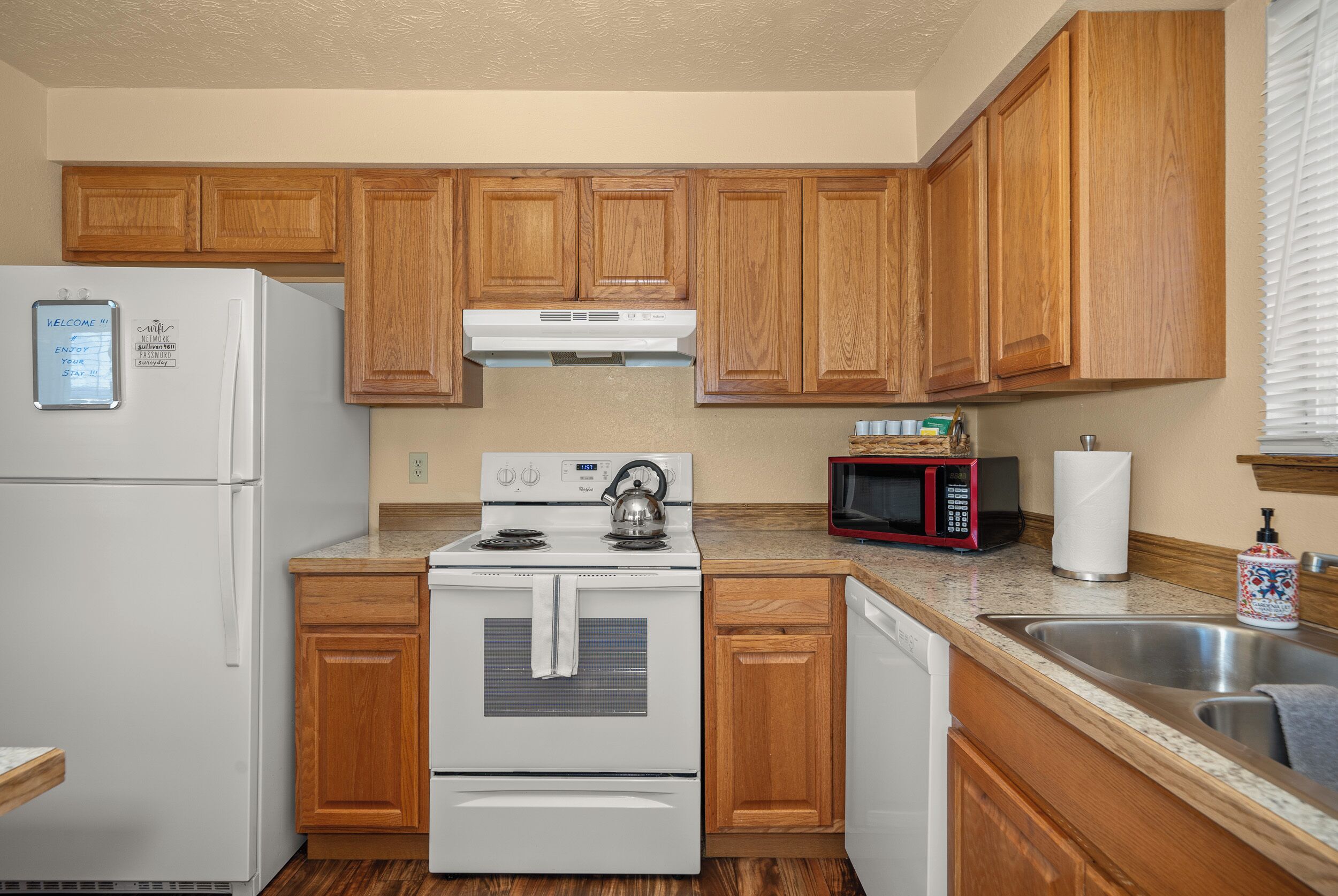A compact kitchen with wooden cabinets, a white refrigerator, a stove, a microwave, and a sink.