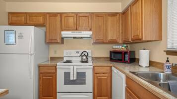 A compact kitchen with wooden cabinets, a white refrigerator, a stove, a microwave, and a sink.