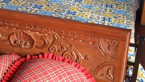 Una cama con colcha estampada, dos almohadas y cabecera de madera con detalles tallados.