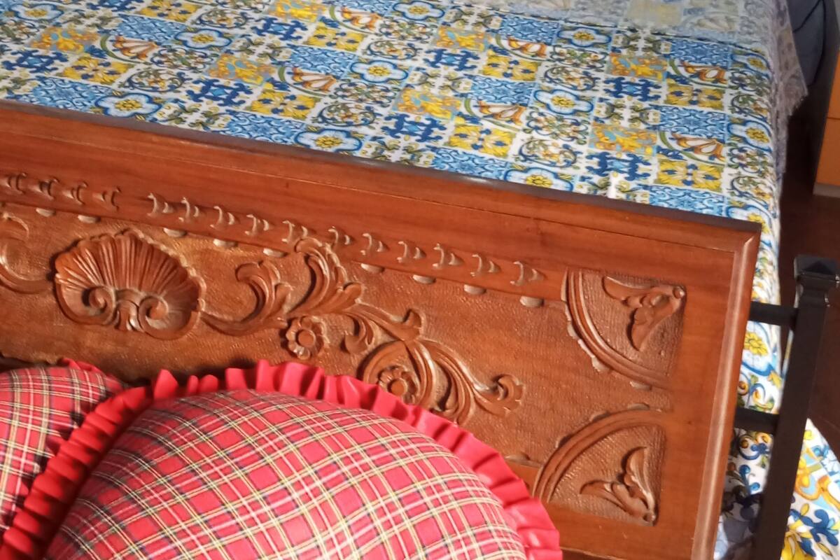 Ein Bett mit einem gemusterten Überwurf, zwei Kissen und einem Holzkopfbrett mit geschnitzten Details.