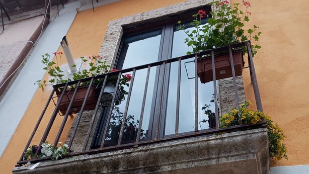 Un balcón con macetas de flores, una ventana y barandilla de metal.