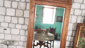 Un espejo con marco de madera, una mesa con sillas y un florero sobre un pedestal.