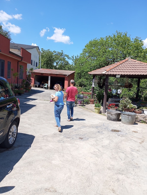 A residential street with houses, a parked car, and a gazebo with potted plants.