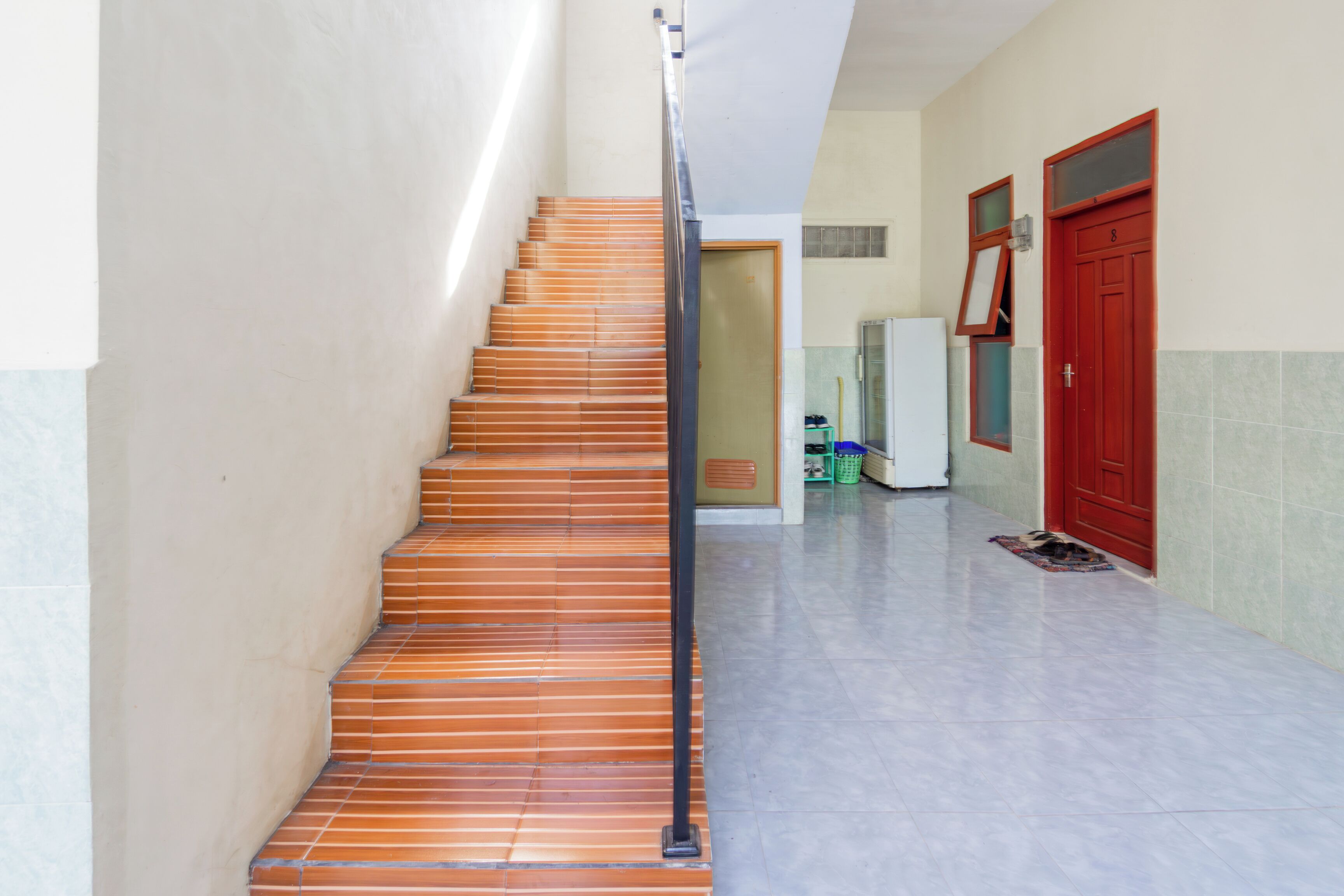 A staircase with wooden steps leading to a landing, a red door, and a refrigerator in the background.
