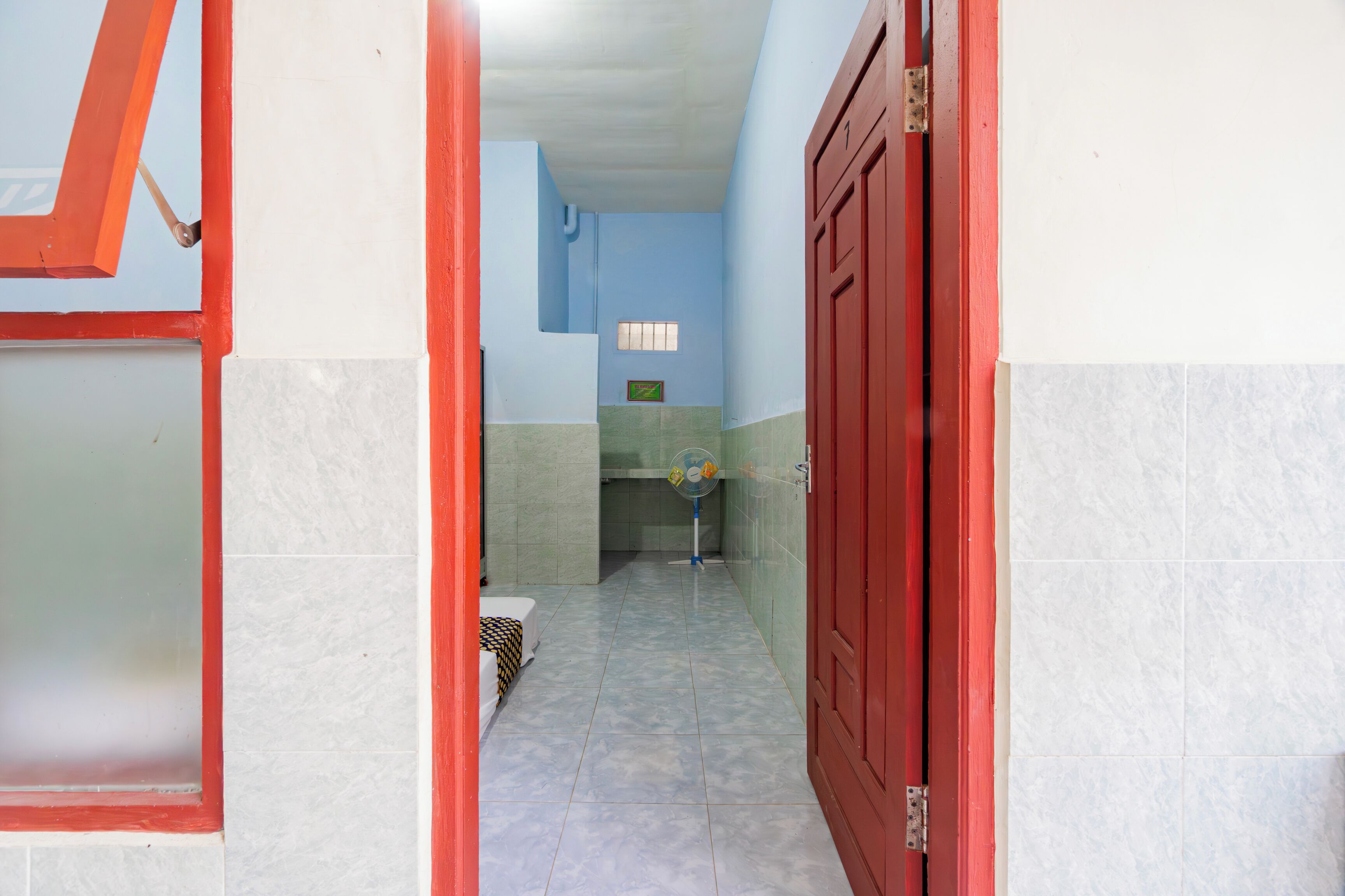 A narrow hallway with tiled flooring, a red door, and a small window.