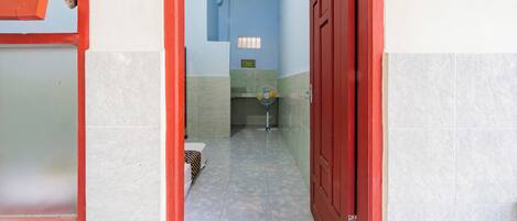 A narrow hallway with tiled flooring, a red door, and a small window.