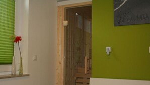 Quarto com cama, parede verde, janela com persianas e porta que dá para uma escadaria.