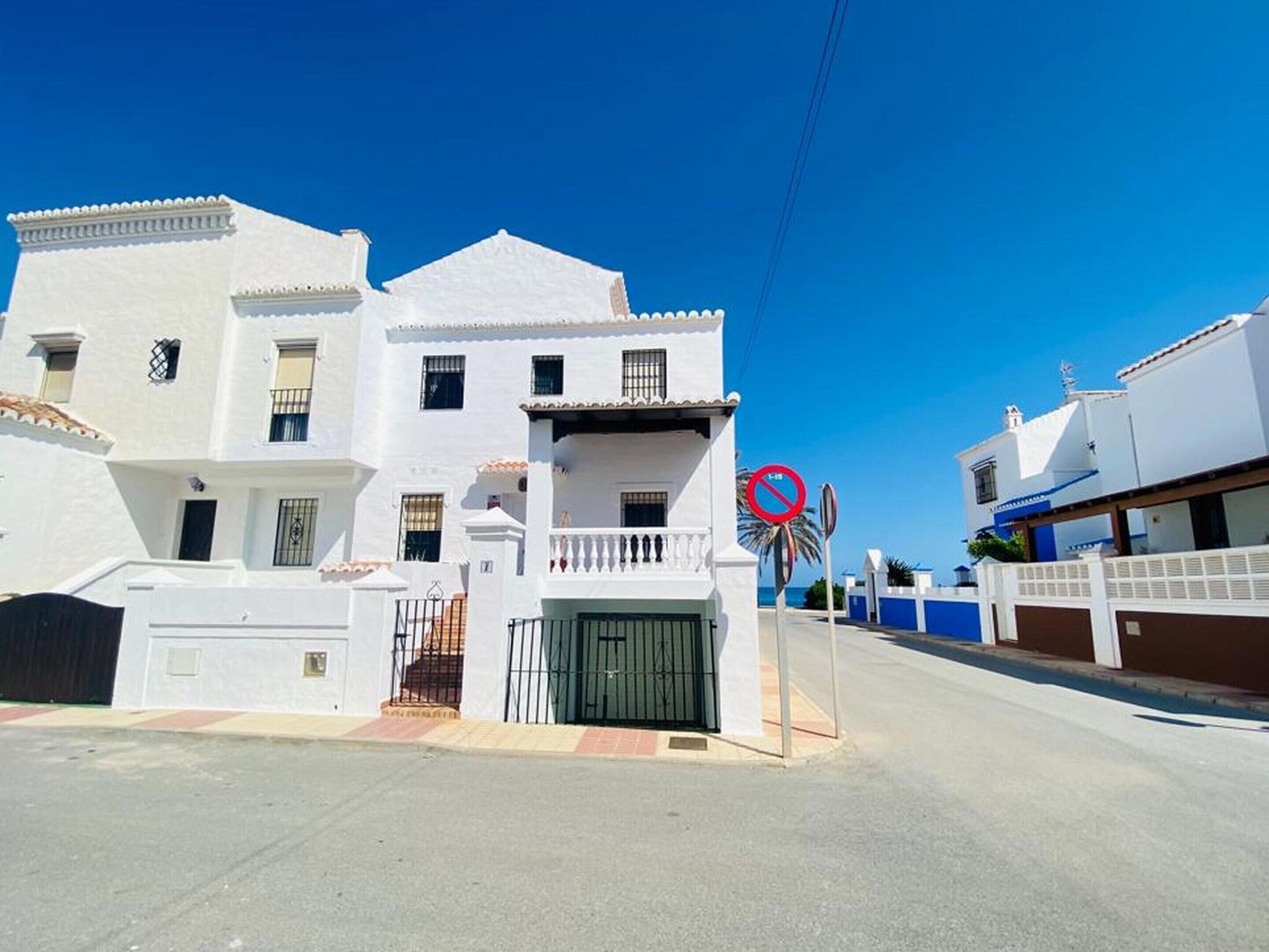 A white two-story building with a gated entrance, a balcony, and a no parking sign.